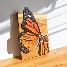 an orange and black butterfly sitting on top of a wooden block next to a white wall