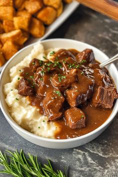 a bowl filled with meat and gravy on top of mashed potatoes