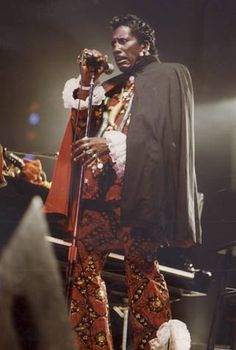 a man standing on top of a stage with a microphone in his hand and an audience behind him