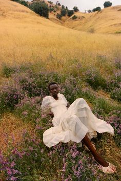 a woman in a white dress laying on the ground surrounded by wildflowers and grass