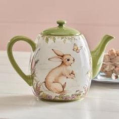 a teapot with a rabbit on it sitting next to a plate full of cookies