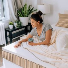 a woman sitting on top of a bed holding a cup