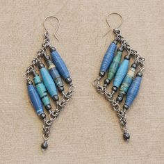 two pairs of earrings with blue beads hanging from the ends of each earring, on top of a beige surface