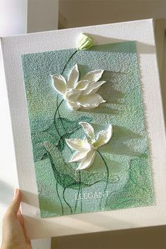 a hand holding up a card with white flowers on green paper in front of it