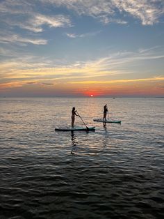 two people stand up paddle boarding in the ocean at sunset or dawn, with one person standing on board