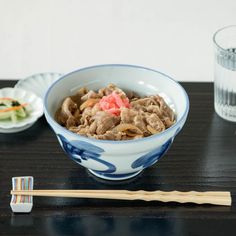 a bowl of food with chopsticks on the side and a glass of water next to it