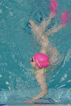 a woman swimming in a pool with a pink frisbee under her arm and head