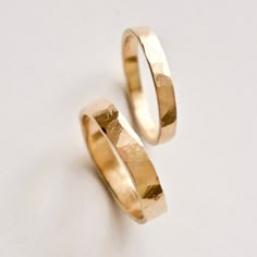 two gold wedding rings sitting next to each other on a white surface with no background