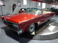 an old red car is on display in a showroom with other classic cars behind it