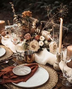 the table is set with white and gold plates, silverware, candles and flowers