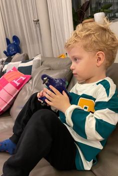 a young boy sitting on top of a couch holding a game controller