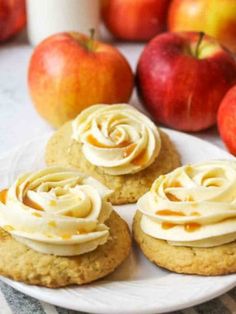 three cookies with icing on a plate next to apples