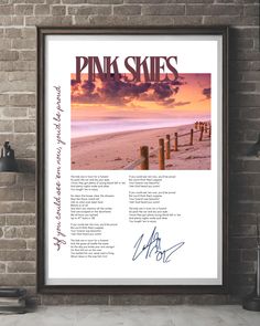 the pink skies poster hanging on a brick wall