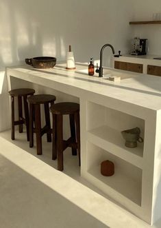 a kitchen with white counter tops and wooden stools next to an open shelf on the wall