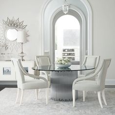 a glass table with chairs around it in front of a white wall and arched window