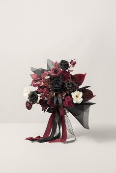 a bridal bouquet with red and white flowers on it's side, tied to a black ribbon