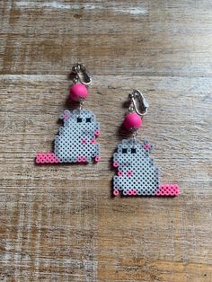 two pairs of pink and silver earrings with an image of a cat on it, sitting on top of a wooden table