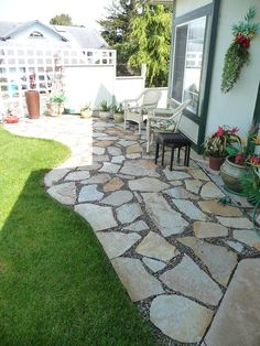 a patio with chairs and plants in the grass near a house that has a white fence