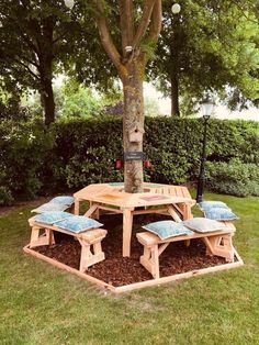 a wooden table and bench under a tree in the grass with blue cushions on it