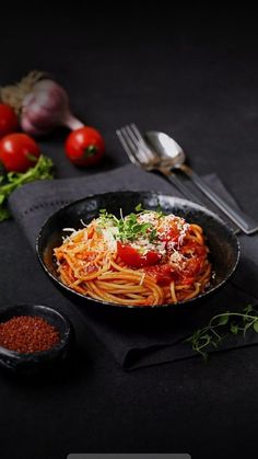 a plate of spaghetti with tomato sauce, parmesan cheese and herbs on the side