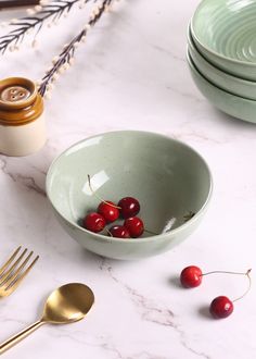 the bowl is filled with cherries on the table next to other plates and utensils