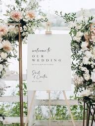 a welcome sign is set up with flowers and greenery for an outdoor wedding ceremony