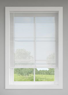 a white window with blinds on it in a room that has grass and trees outside the window