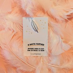 a white feather pin is on top of some pink and white feathers with a quote