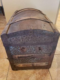 an old wooden chest sitting on top of a tile floor next to a white wall