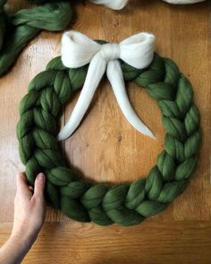 someone making a wreath out of yarn on a wooden table with white ribbons and bows