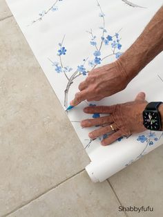 an older man is painting on the floor with blue flowers and white paper while holding his watch