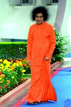 a woman in an orange dress is walking down the blue carpeted walkway with flowers behind her