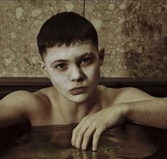 a man with white paint on his face sitting in a bathtub looking at the camera