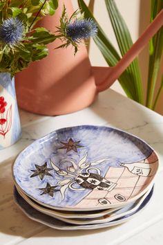 a stack of plates sitting on top of a table next to a potted plant