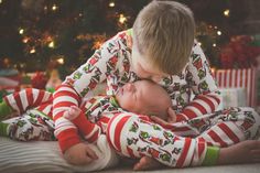 two children in matching christmas pajamas laying on the floor next to a christmas tree with presents