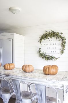 three pumpkins sitting on top of a table in front of a white kitchen wall