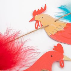 some red and blue feathers are hanging from a string on a white surface with an orange bird