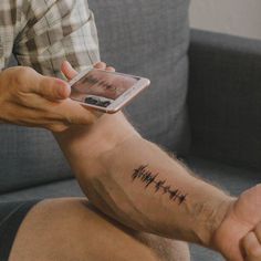 a man is holding his cell phone and has a heartbeat tattoo on his left arm