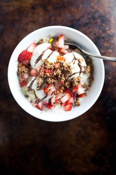 a white bowl filled with granola and strawberries on top of a wooden table