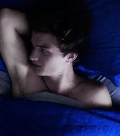 a young man laying in bed with his head on the pillow while looking at something