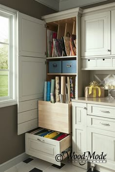 a kitchen with white cupboards and drawers filled with books, magazines and other items