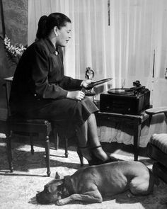 a woman sitting in a chair next to a dog on the floor near a table