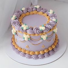 there is a purple cake with white flowers on the top and gold trimmings