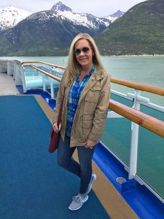 a woman standing on the deck of a cruise ship with mountains in the back ground