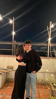 a man and woman standing next to each other on top of a roof at night