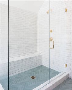 a walk in shower sitting next to a white tiled wall and floor with gold fixtures