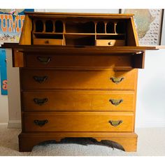 an old fashioned wooden desk with drawers on the top and bottom drawer, in front of a poster