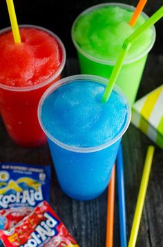 three different colored drinks sitting next to each other on top of a wooden table with candy bars