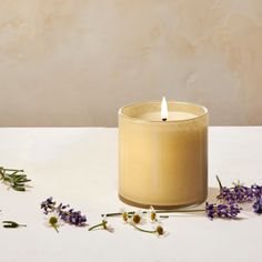 a lit candle sitting on top of a white table next to lavenders and flowers