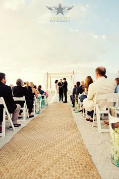 a wedding ceremony on the beach with people sitting in chairs and one person standing at the end